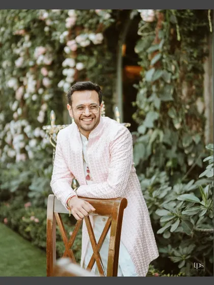 A handsome portrait of the groom, smiling in a garden setting. This shot captures his happiness and stylish wedding attire.