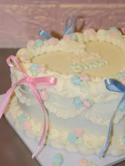 A close-up of the heart-shaped baby shower cake, focusing on the delicate ribbon details and soft color palette.