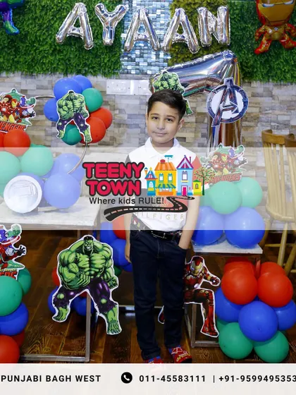 The birthday boy posing proudly in front of his Avengers-themed party setup.