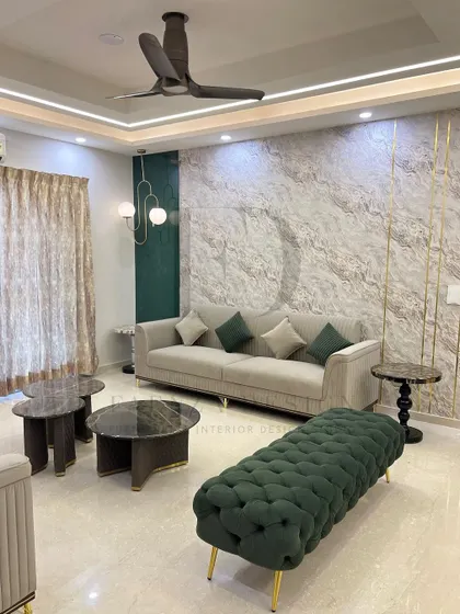 A harmonious blend of olive green and beige. This living room features a beige sofa, a woven green ottoman bench, and a marble-clad accent wall with gold-toned metal inserts for a touch of glamour.