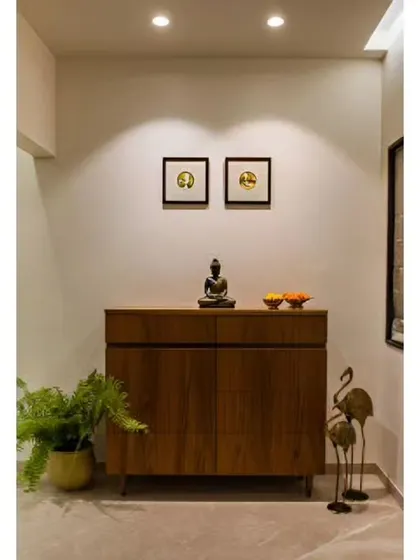 A simple yet elegant foyer with a wooden storage cabinet, a potted fern, and minimalist art on the wall. Spotlights highlight the decor, creating a calm and welcoming vibe.