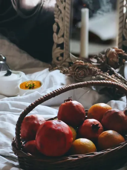 A more focused shot on the basket of pomegranates and oranges, with candles and dried roses in the background. The lighting is soft and moody, creating a vintage, romantic feel.