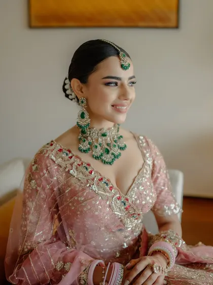This bride was pretty in pastels. We created a soft, romantic makeup look with a hint of shimmer on the eyes to complement her pink lehenga and emerald jewelry.