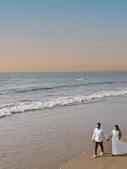A wide aerial shot of a couple walking hand-in-hand along a deserted beach at sunset. Drone photography allows me to capture the vastness of the landscape and the intimacy of the moment simultaneously.