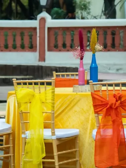 A vibrant table setup with a yellow tablecloth and chairs adorned with bright orange and yellow sashes, perfectly fitting the carnival theme.