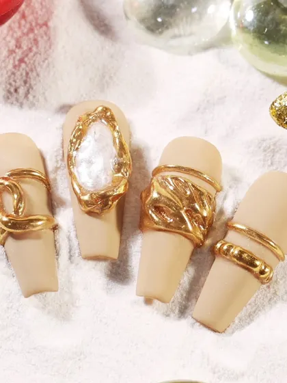 The gold molded nail art displayed on a sand-like texture, emphasizing the luxurious, treasure-like quality of the design.
