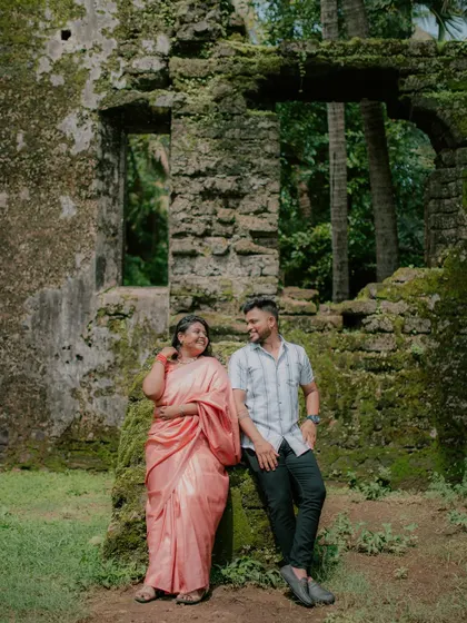 A full-length portrait of a couple posing against moss-covered stone ruins.
