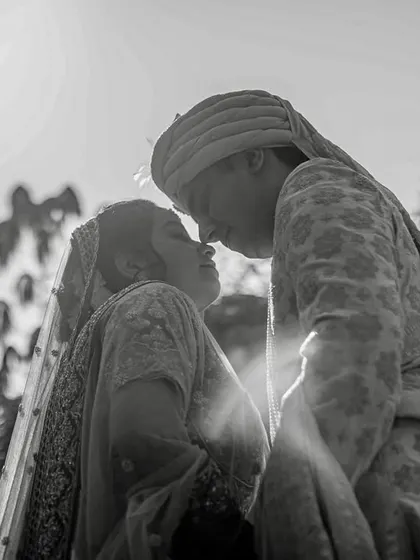 The same intimate moment as the previous shot, rendered in dramatic black and white. The backlighting creates a beautiful silhouette effect, emphasizing their connection.