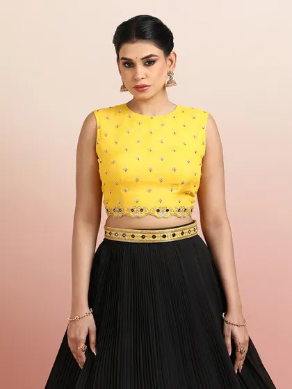 A close-up of the yellow embellished blouse, featuring delicate buti work and a scalloped mirror-work border.