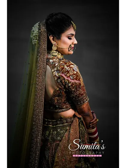An elegant and moody bridal portrait. The side profile and studio-like lighting highlight the intricate details of her hair, makeup, and the back of her blouse.