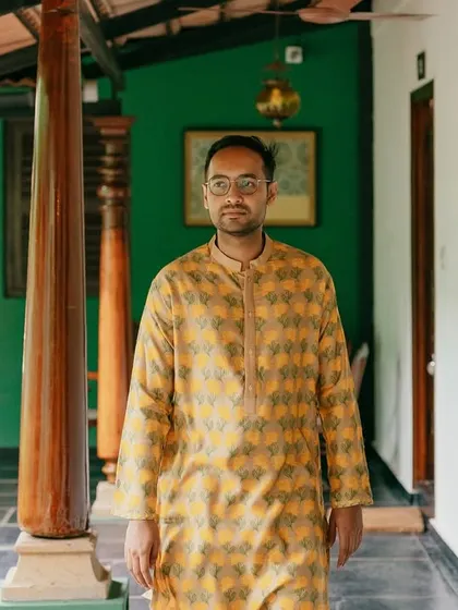 The groom, in a yellow printed kurta, walks along the verandah, a relaxed and handsome portrait.