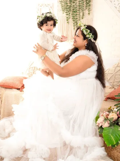 A mother and daughter, both crowned with flowers, share a happy moment.