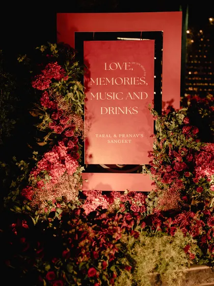 Every event needs a clear story. This custom sign, framed in red florals, set the mood for the sangeet: a night of 'Love, Memories, Music and Drinks.'
