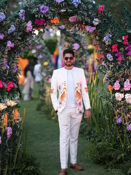 Here is one of my custom bandhgala jackets, seen at a beautiful garden wedding. The crisp white fabric is the canvas for a hand-painted floral and bird motif, designed to complement the festive atmosphere. This is how you make a statement with elegance.