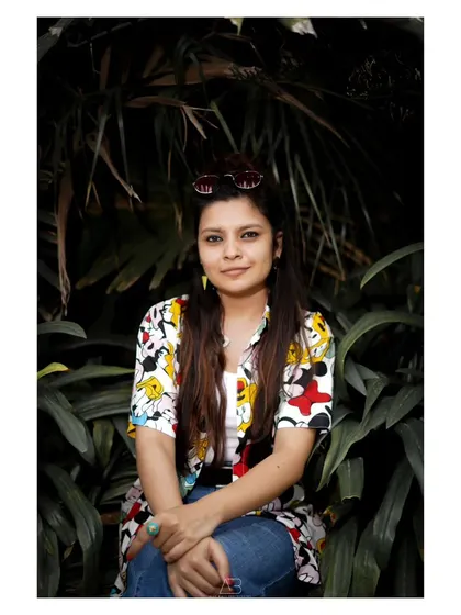 A relaxed portrait in a park. The dark, leafy background makes her colorful shirt and her expression the focus of the image.