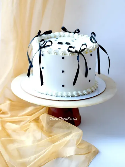 A side view of the classic vintage cake, showing the delicate black ribbon bows and heart details on the smooth white buttercream.