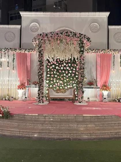 A classic and romantic outdoor wedding stage. The structure is adorned with pink and white florals, with a beautiful floral chandelier centerpiece hanging above the main seating.