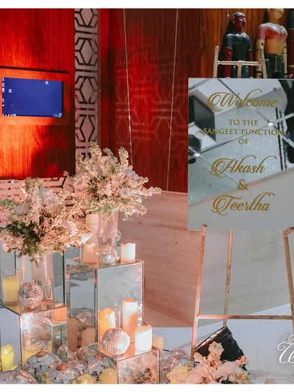 A welcome setup for a Sangeet, where mirrored pedestals, candles, and floral arrangements create an ambiance of modern glamour and warm hospitality.