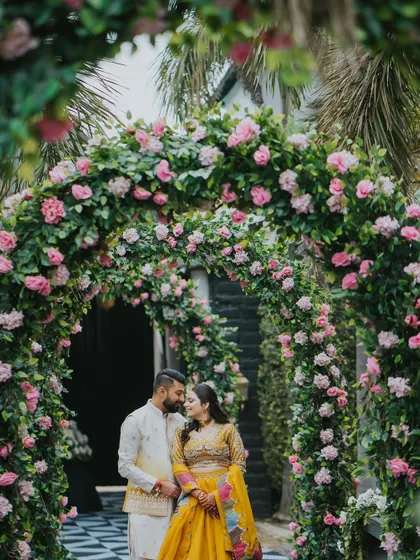 A couple shares a moment under a dense archway of pink roses, creating a romantic and intimate portrait.