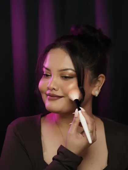 A shot of me applying blush, showing the technique for a natural, flushed look. The purple background adds a pop of color and mood.