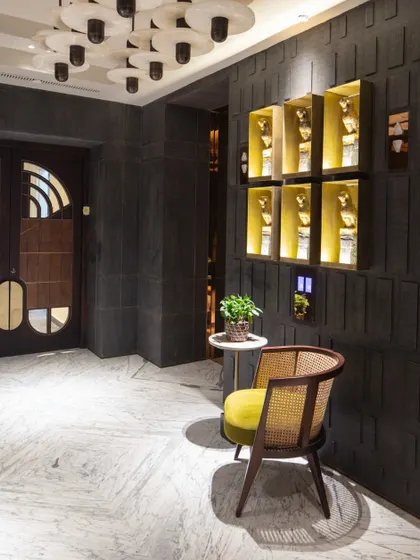The lift lobby is designed as a gallery space, with honed granite walls and niches displaying a ceramic horse installation by Partha Dasgupta. A single cane chair adds a touch of warmth and organic texture.