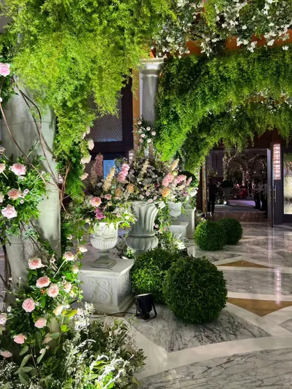 The entrance hallway, with marble floors and pillars adorned with climbing pink roses and overflowing greenery, creating a luxurious and romantic welcome.