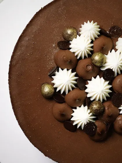 A top-down view of a beautifully decorated chocolate cake, showing the contrast between the rich chocolate mousse and the piped white cream.