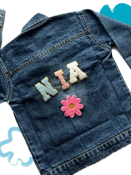 A simple and cute custom denim jacket for a girl named "Nia," featuring her name and a flower patch.