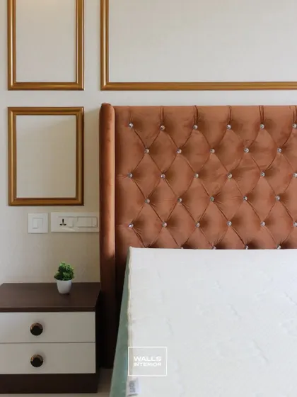 A close-up of a luxurious, button-tufted headboard in a rich brown velvet. The wall behind features elegant gold-colored molding, adding a touch of classic grandeur.