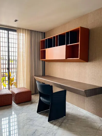 This study nook within a bedroom features a minimalist wall-mounted desk and orange cabinetry for a pop of color. The space is designed for focus and creativity, with soft natural light filtering through sheer curtains.