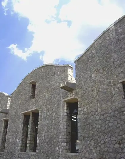 The exterior of the Synergy Textiles Factory is built with local stone, providing a robust and thermally efficient building envelope. The curved roofline softens the building's form and is a signature element of this climate-responsive industrial design.