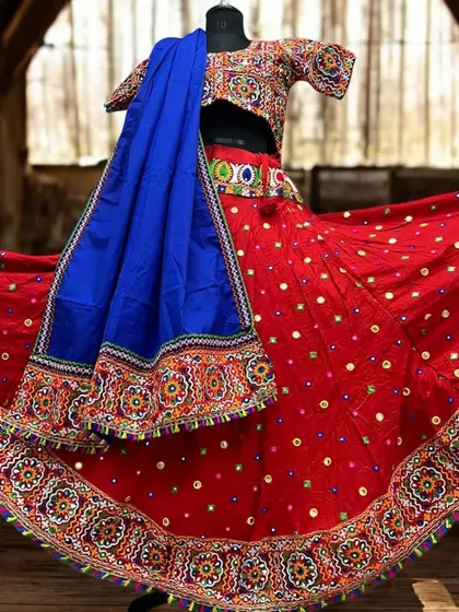 A classic red chaniya choli with intricate multi-color embroidery and mirror work along the border. The contrasting royal blue dupatta makes the entire outfit pop.