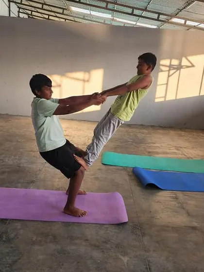 In the warm sunlight, two campers practice a standing partner balance, a great exercise for building leg strength and core control.