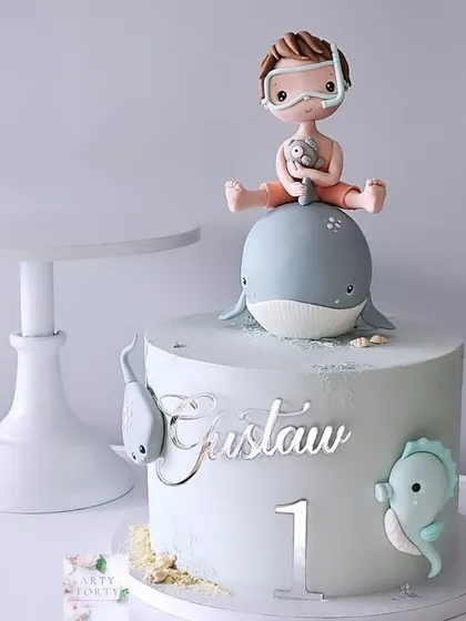 A minimalist sea-themed cake with a boy and his whale friend. This design uses a soft, pastel color palette for a gentle and sweet first birthday cake.