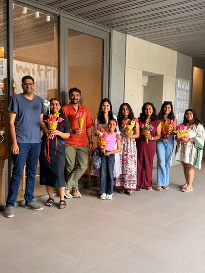 A smiling group of participants, including adults and a child, pose together holding the beautiful origami flower bouquets they created during our workshop. These sessions are great for all ages and leave everyone with a handmade treasure.