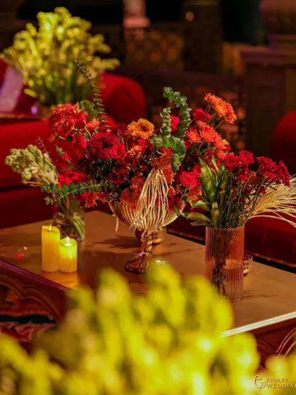 A table setting with a lush floral centerpiece and warm candlelight. In the background, the plush red velvet seating of the Sufi lounge creates a cohesive and immersive environment.