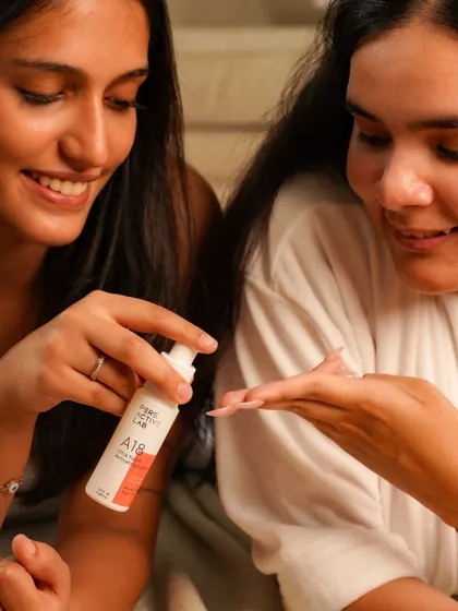 A candid shot of two women enjoying a skincare product together. The natural smiles and shared experience make the brand feel approachable and perfect for a relaxing self-care routine with friends.