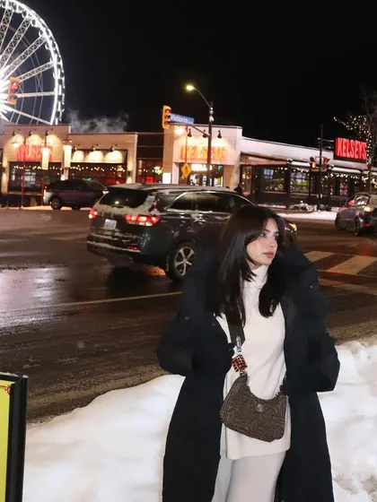 A full view of my cozy winter outfit against the snowy streets and bright lights of Clifton Hill.
