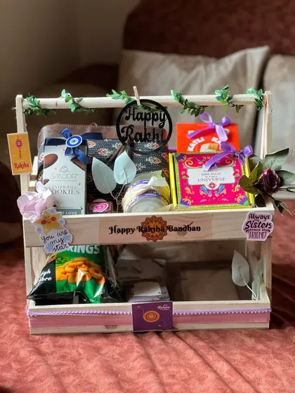 A neatly arranged two-tiered Rakhi hamper with a "Happy Rakhi" sign, perfect for a sister.