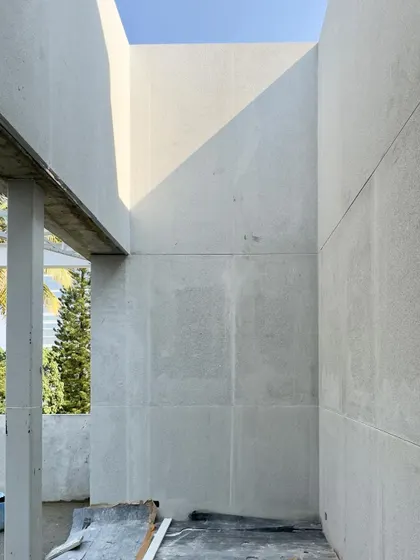 A light-well under construction, with the sun creating a sharp diagonal line on a raw concrete wall.