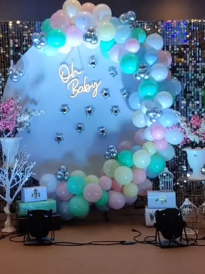 An elegant baby shower setup with a shimmering sequin backdrop, a circular frame with pastel balloons, and a neon "Oh Baby" sign.