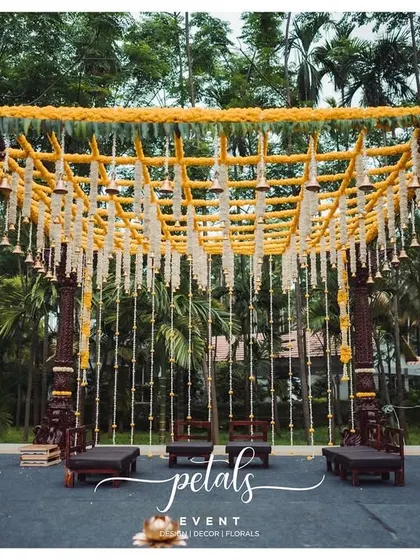This Kerala-style mandap is a testament to timeless traditions. The intricately carved wooden pillars, combined with a canopy of chrysanthemums and temple bells, create a space that is both majestic and sacred.