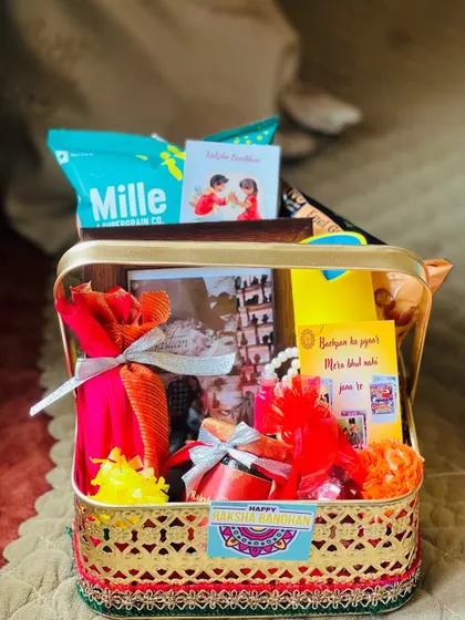 A Raksha Bandhan hamper in a golden basket, personalized for a brother. It includes a photo frame, snacks, and a heartfelt note.