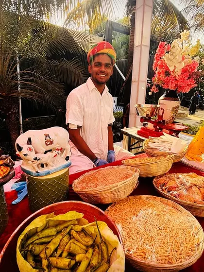A rustic 'namkeen' or savory snack counter set up for a festive occasion. It features a variety of traditional Indian fried snacks, chutneys, and garnishes for guests to create their own mix.