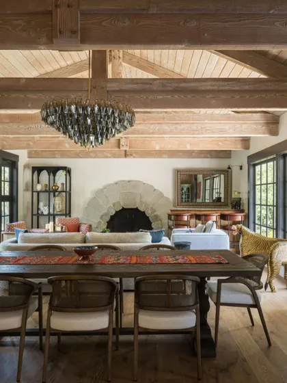 A wide shot of the open-plan living and dining area in the Saratoga home. The design emphasizes a sense of space and light, with the vaulted, beamed ceiling creating a feeling of grandeur. The tiger-shaped chair adds a touch of playful drama.