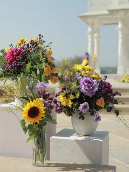 A beautiful arrangement of sunflowers and purple roses, with the white marble pillars of the mandap in the background.