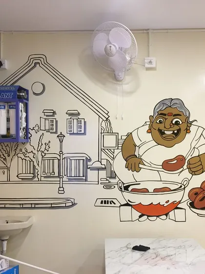 A fun, character-based illustration of a woman making vadas, painted for a local eatery. This cartoon style adds personality and warmth to the restaurant's interior.
