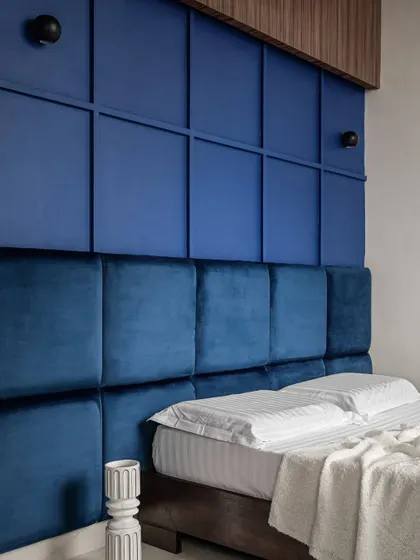 The headboard wall features a grid of upholstered blue panels, creating a strong, graphic statement. The design is modern, comfortable, and full of character.