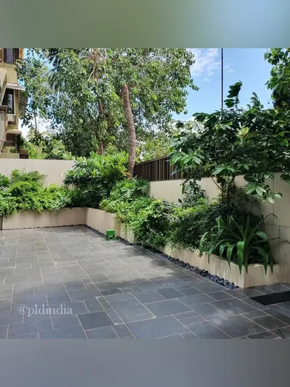 An open patio space bordered by lush garden beds. This design provides a functional area for outdoor living while being surrounded by the beauty and privacy of a dense garden.