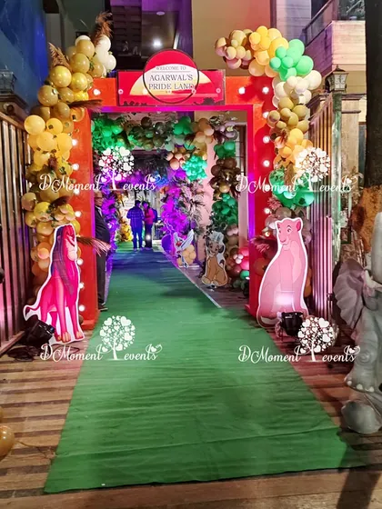A grand jungle entrance for a "Lion King" themed party, featuring a green carpet walkway lined with animal props and a custom "Pride Land" sign.